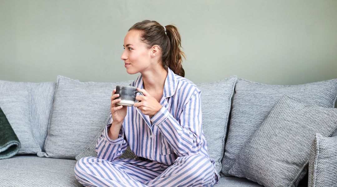 Woman wearing a cute pj set on the couch while drinking coffee