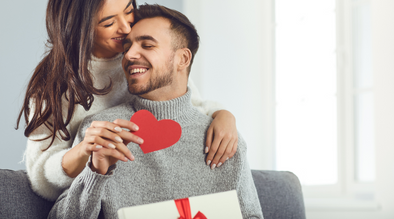 A woman hugging a man who is seated. They are celebrating Valentines Day.