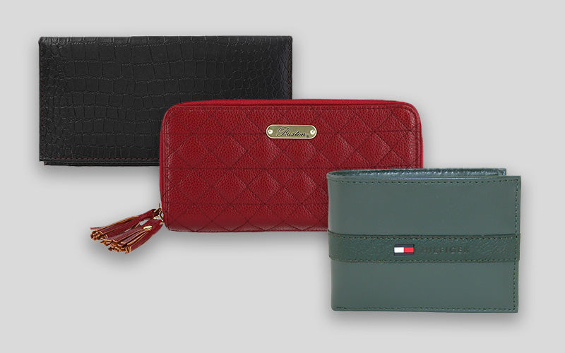 Three wallets displayed at an angle. The one in the back is black, the one in the middle is red with a tassel zipper, and the front wallet is a sage green.